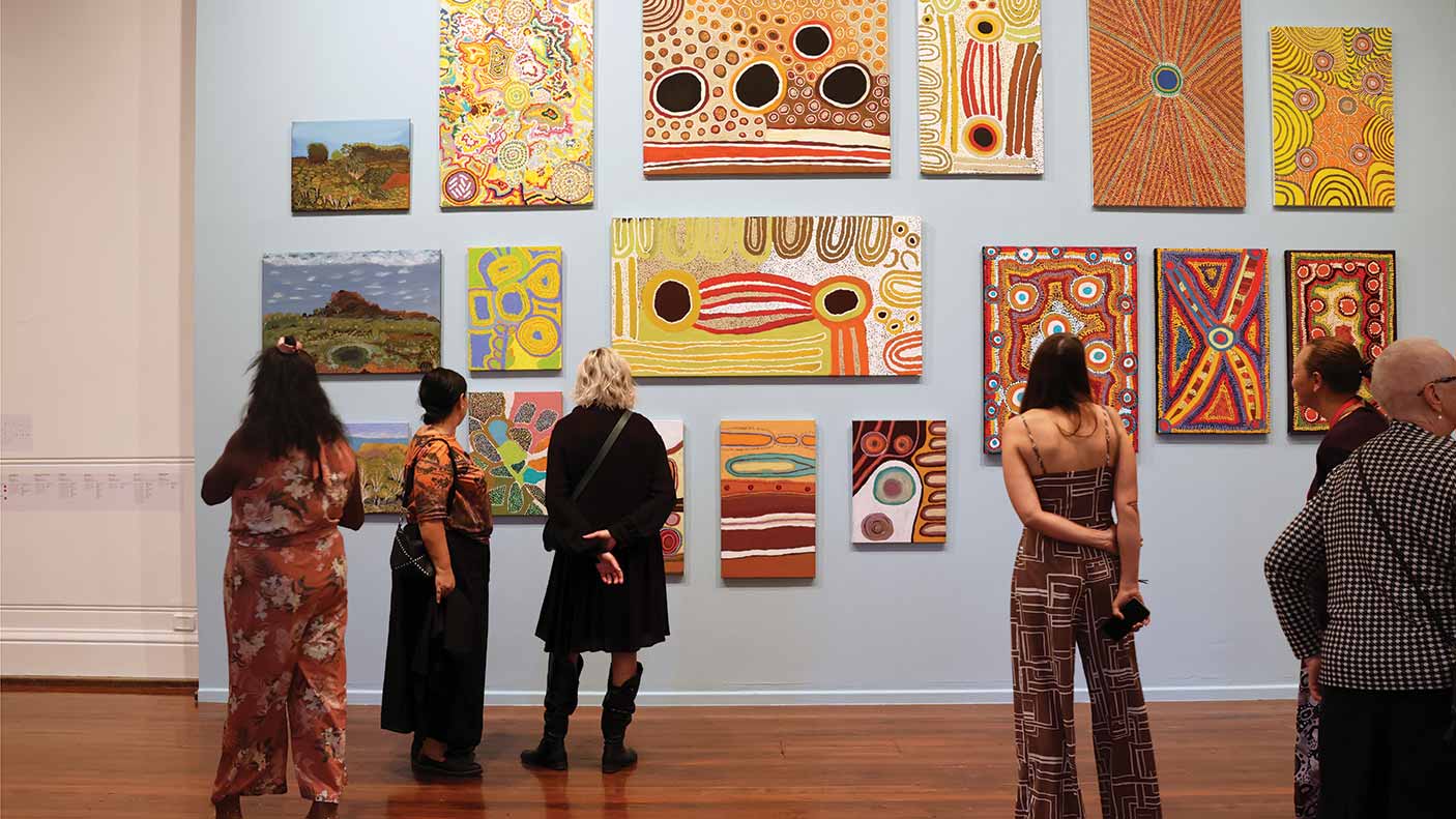 A small group of people stand in an art gallery looking at the Aboriginal artworks on display.