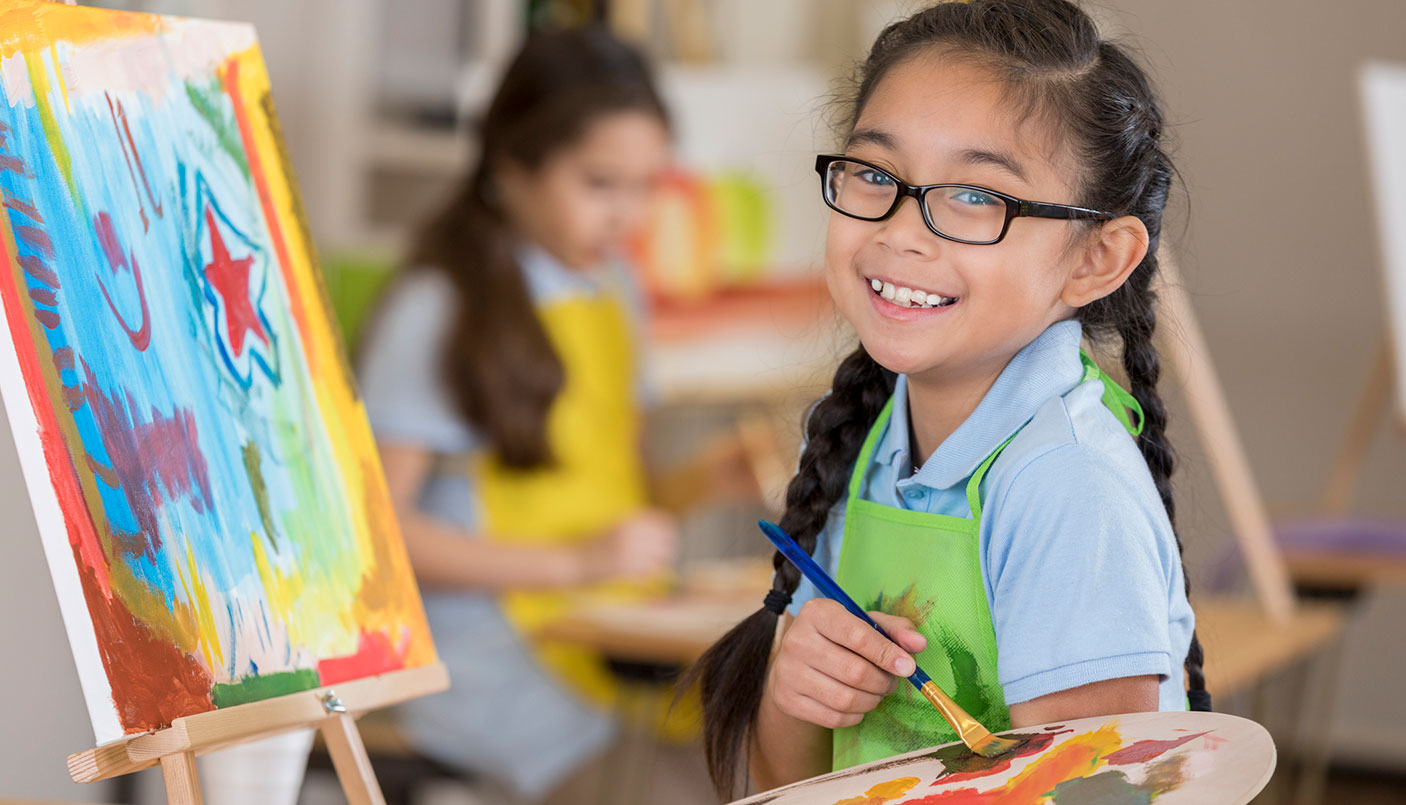 A young girl holds a painting palette and creates a painting resting on an easel