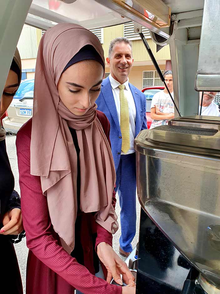 A woman using a coffee machine with the Minister in the background