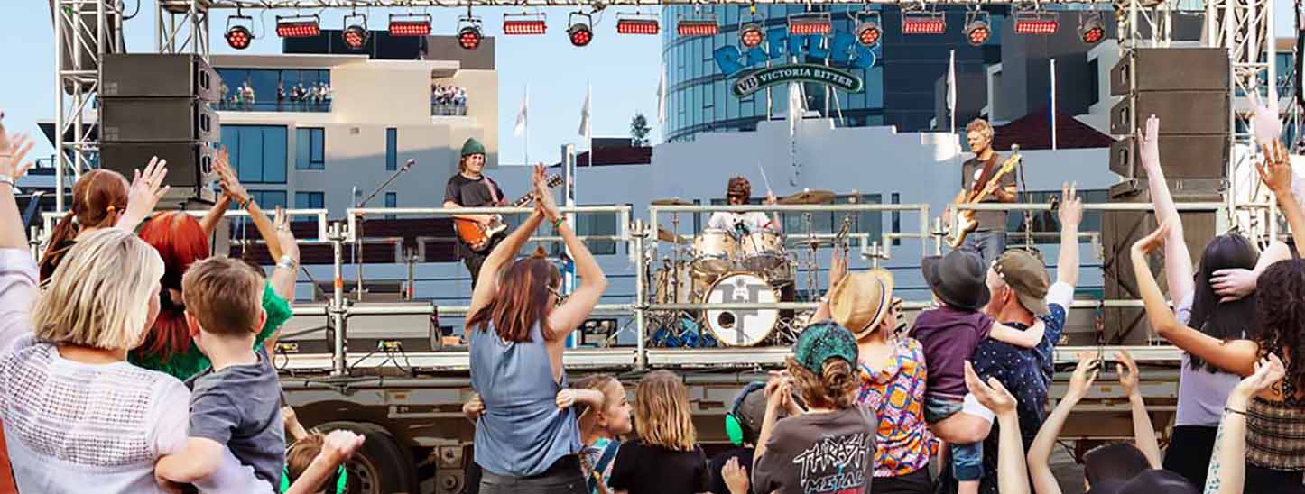 A crowd cheering a band on stage with the Raffles Hotel in the background