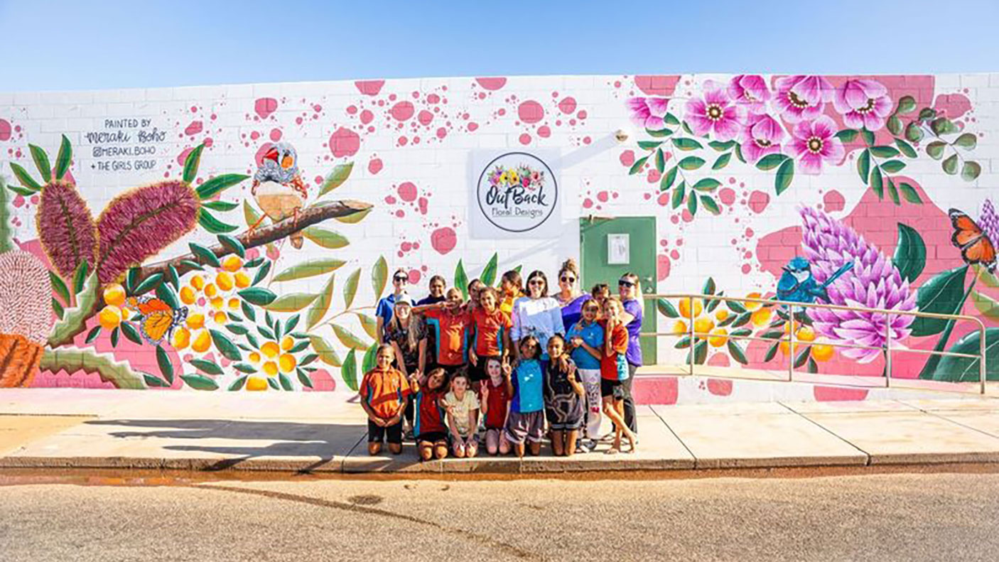 A group of young people stand in front of a colourful wall mural