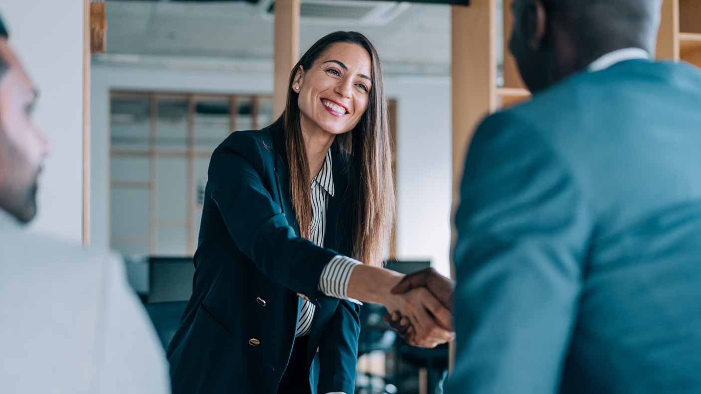 Woman stands up and shakes the hand of a business colleague