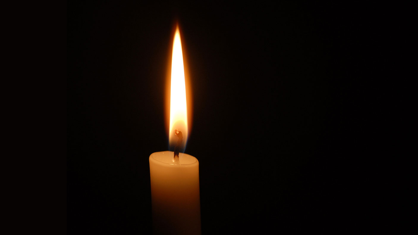 A single candle and flame, against a black background