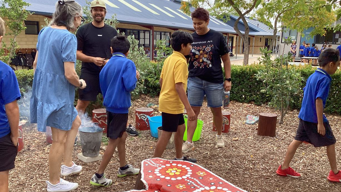 A group of school children walking around an Aboriginal artwork during a smoking ceremony.