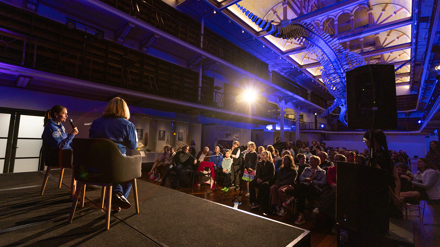 Two ladies sitting on chairs on a stage talking to an audience of children and adults.