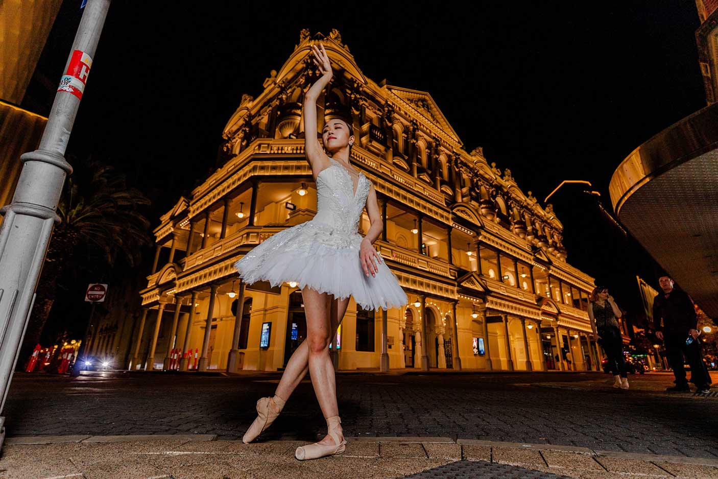 A ballerina in front of His Majesty's Theatre at night. The theatre is lit up at night.