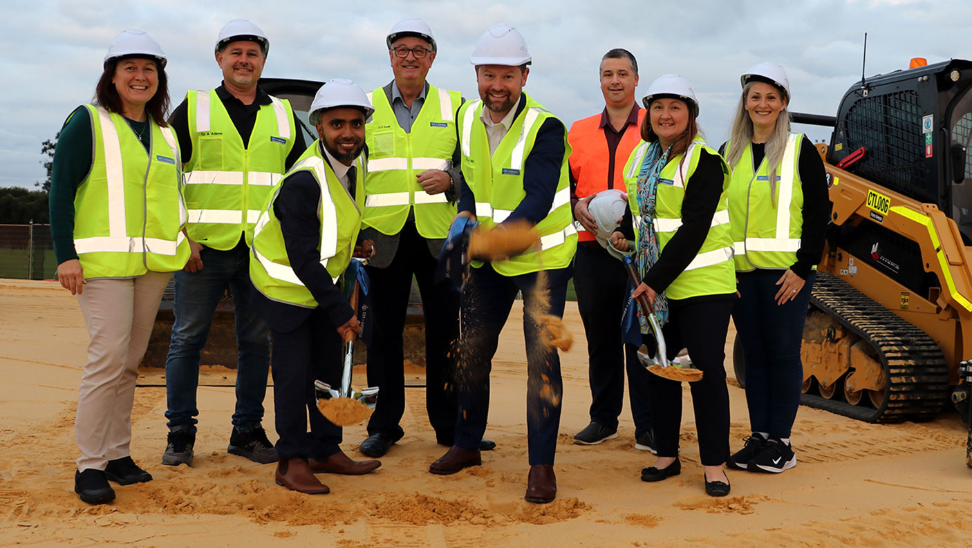 8 people in hi-vis vests pose for a photo while 3 of the group  turn the first sod for the development of the Youth Entertainment  Space