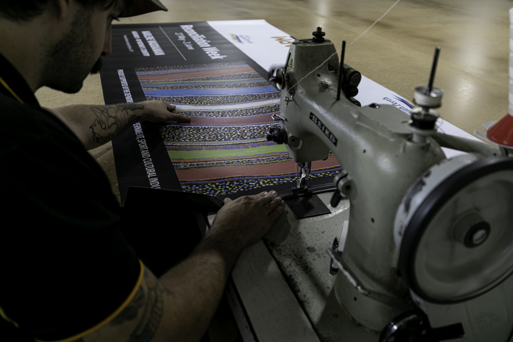 A man sewing a banner with Aboriginal artwork
