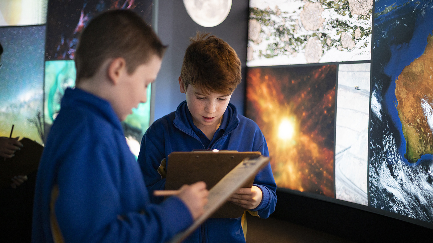 Two students taking notes in front of an exhibition of images taken from space.