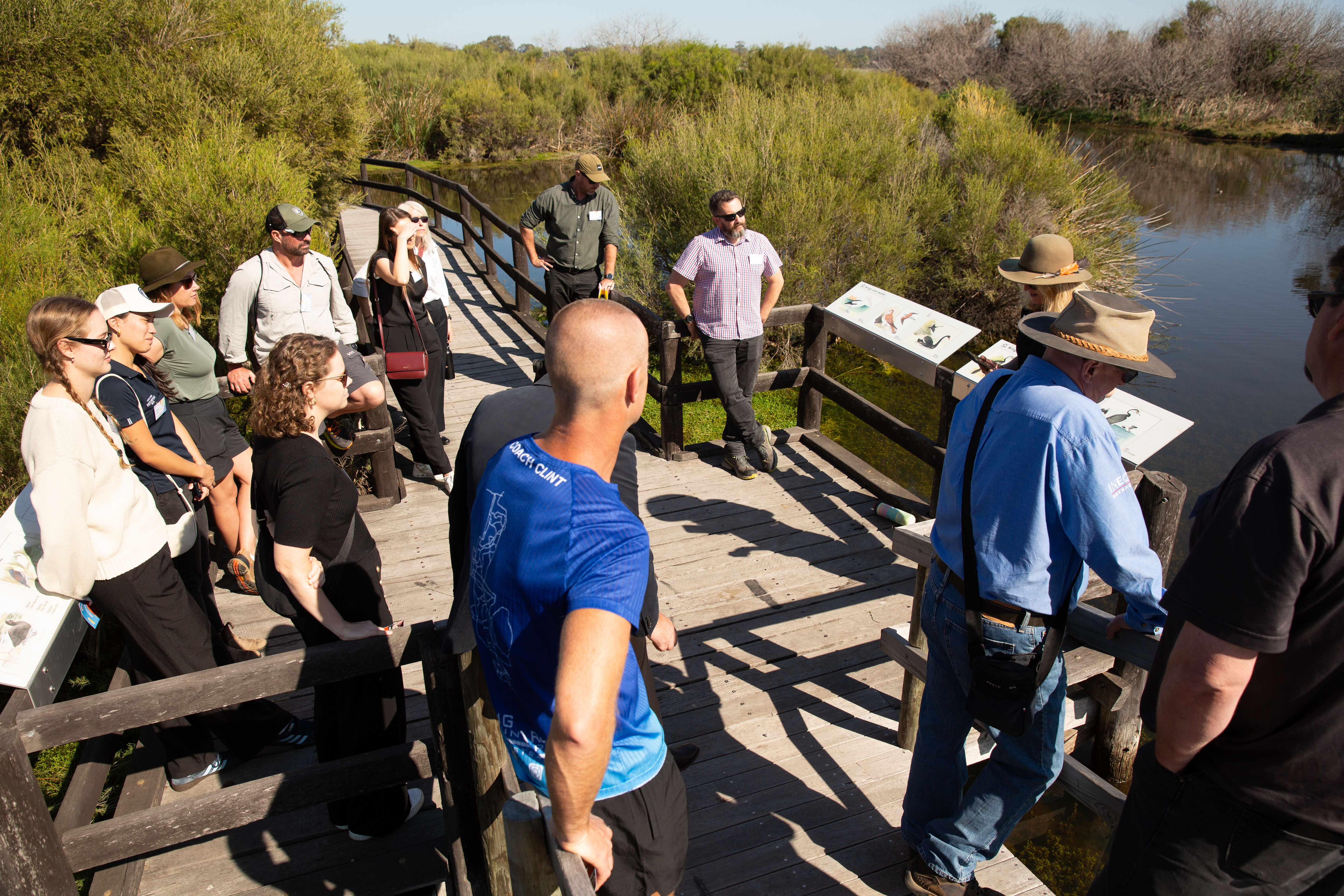 A group of people on a guided bushwalk, standing on a bridge over a river.