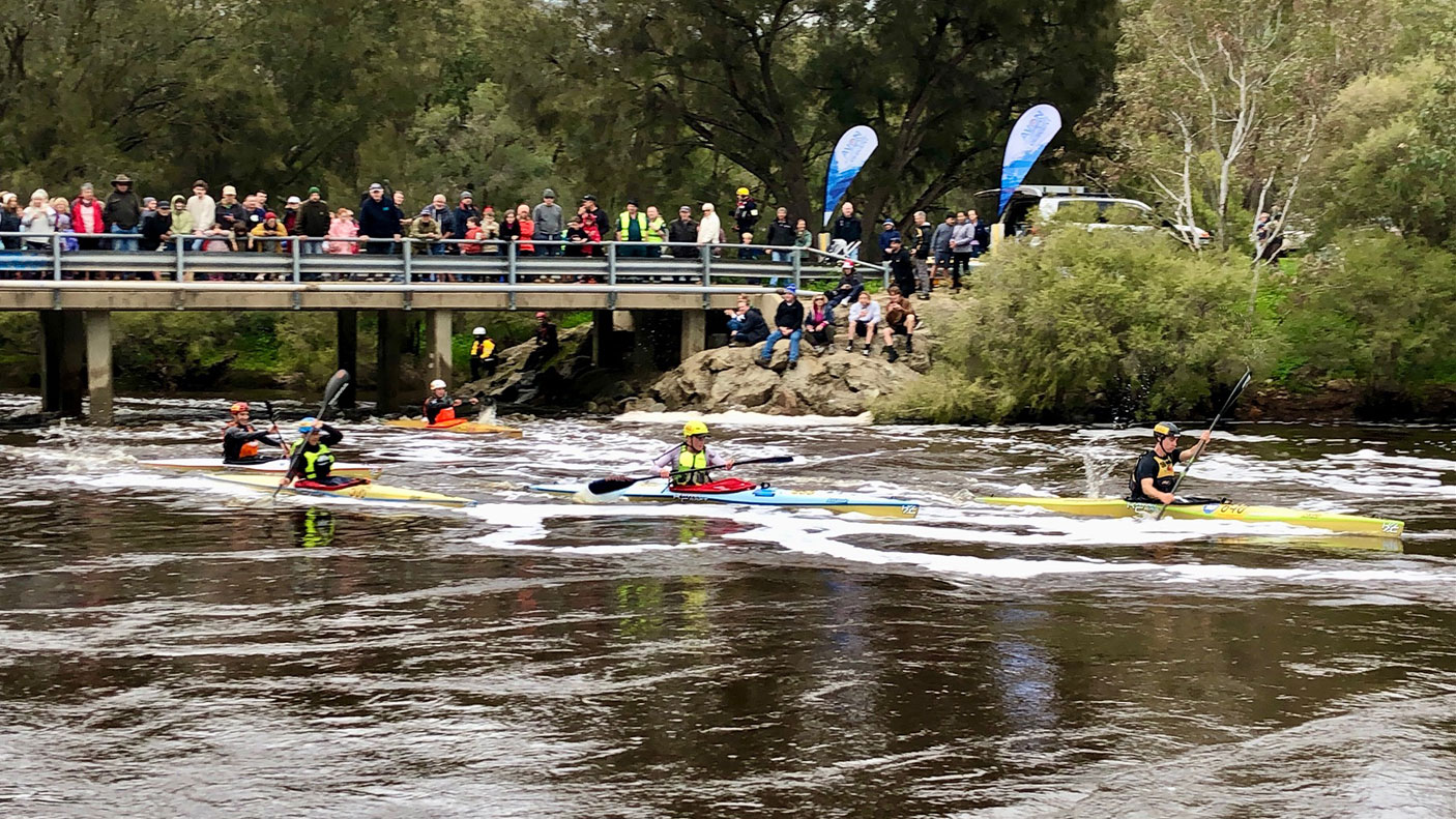 Paddles at the Avon Descent pass under a pedestrian bridge with people watching the race.