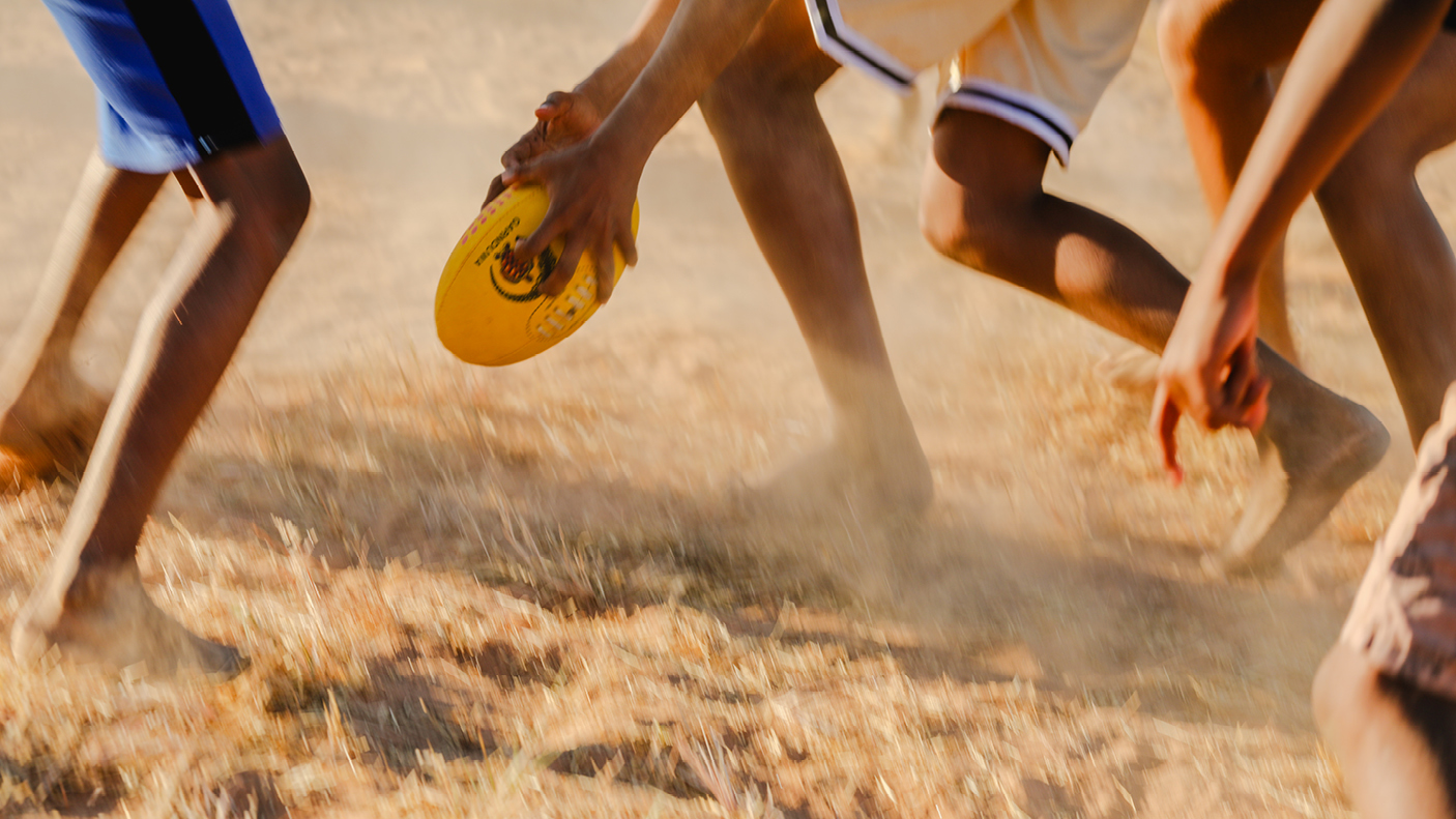 Young people playing rugby on a dirt sporting field