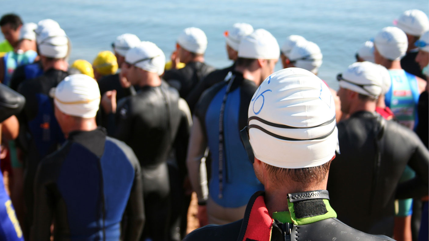 A group of swimmers about to start an ocean race. All wearing swim caps, goggles and racing attire