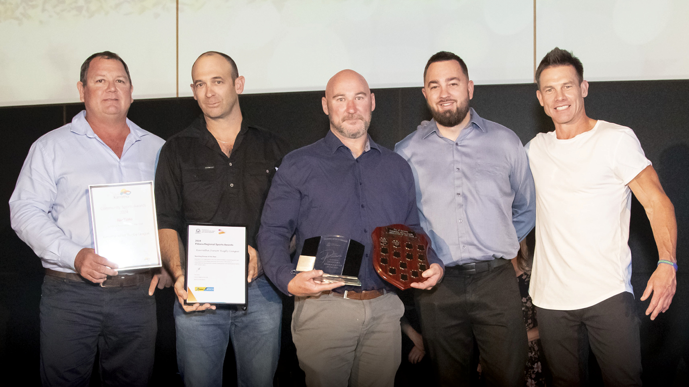 5 men stand whilst holding trophies and certificates